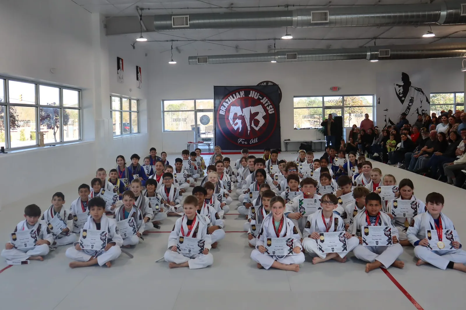 A kids class seated in rows in the bright mat room at G13 Cary